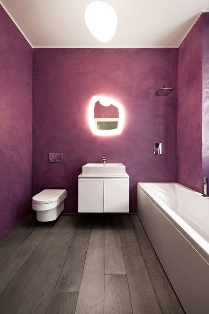 a minimalist bathroom with purple walls, a wooden floor and white appliances and a catchy shaped mirror