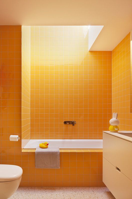 a minimalist bathroom with sunny yellow square tiles all over the space, a floating vanity with a sink and a skylight that fills the room with natural light