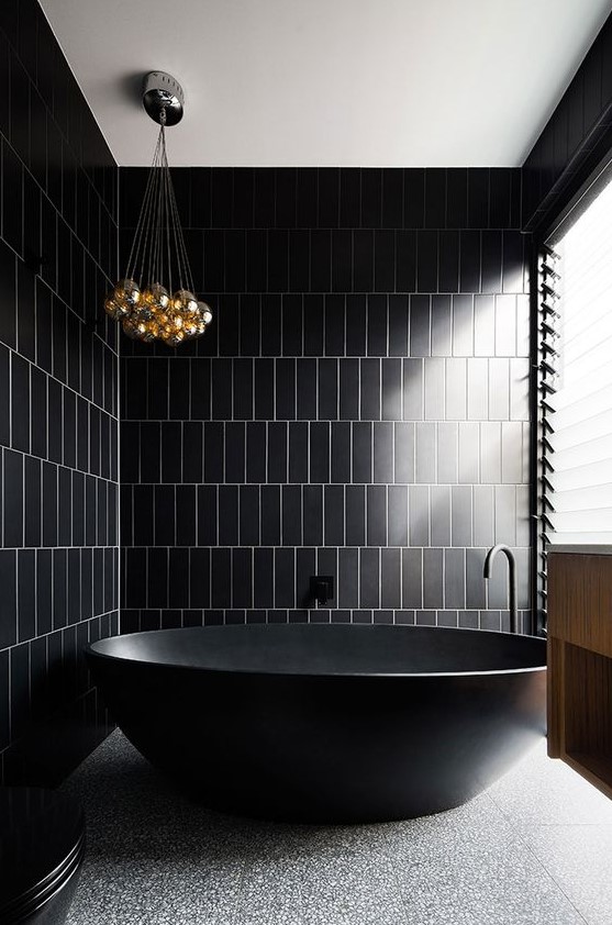 a minimalist black and gold bathroom with a stone floor, a bubble chandelier and a pretty free standing tub