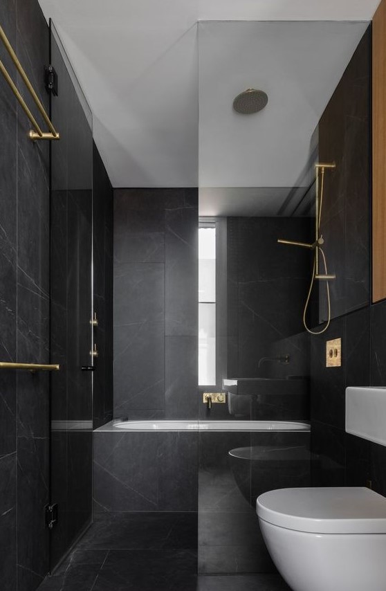 a minimalist black and gold bathroom with black marble tiles, gold fixtures and white appliances is super stylish