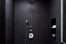 a minimalist black bathroom clad with large scale and chevron black tiles, a skylight and neutral fixtures is cool