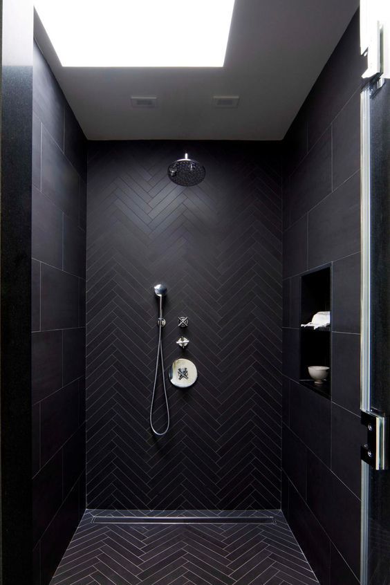 a minimalist black bathroom clad with large scale and chevron black tiles, a skylight and neutral fixtures is cool