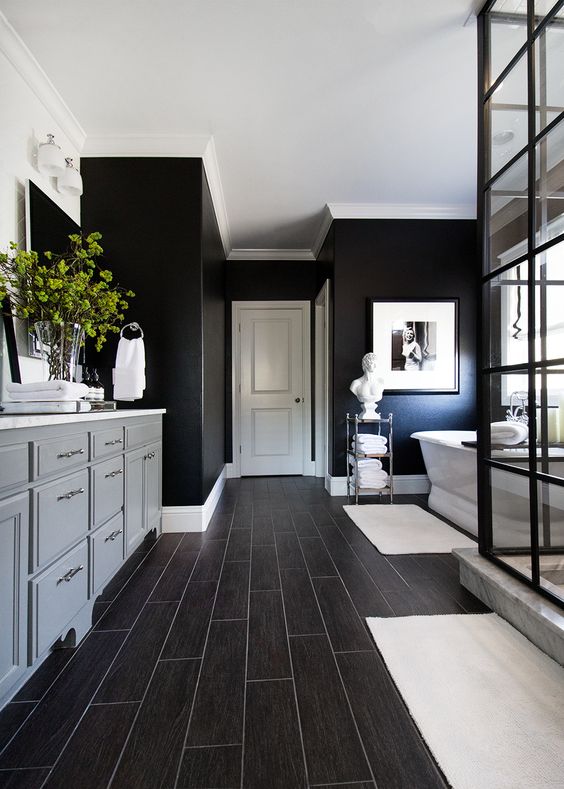 a modern farmhouse black bathroom with blakc walls, a white tub, a grey vanity, dark laminate and a shower enclosed in glass