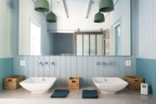 a modern light blue bathroom with beadboard, a concrete vanity and green pendant lamps over the sinks