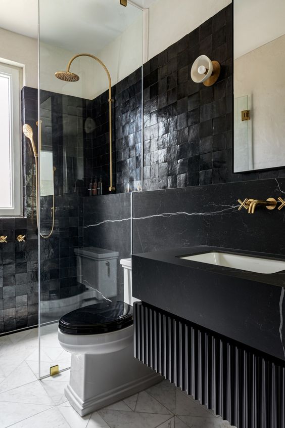 a modern moody bathroom with catchy tiles and black marble, a floating vanity, gold fixtures and a mirror