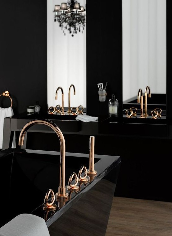 a modern refined bathroom with black sinks, a black sculptural tub, a chic black chandelier, gold fixtures and large mirrors