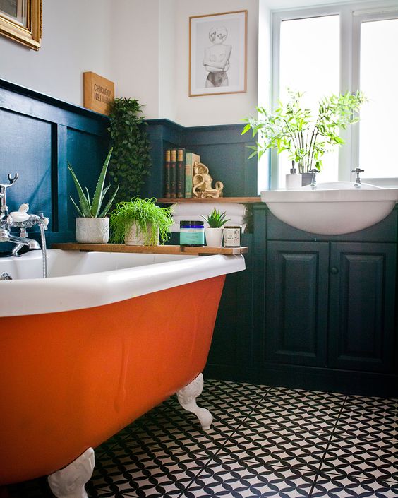 a monochromatic bathroom spruced up with a bright orange bathtub and potted greenery that refresh the space and make it bolder