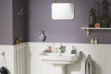 a moody modern farmhouse bathroom with purple walls, white paneling, a free-standing sink and vintage shelves