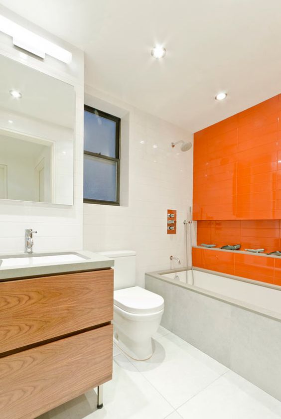 a neutral contemporary bathroom with white tiles, concrete and wood and a statement orange tile wall