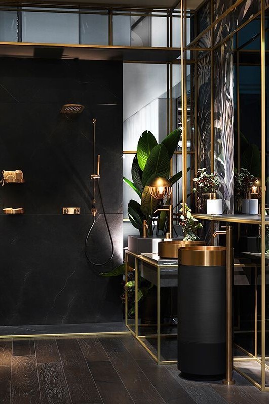 a refined modern bathroom done in black and gold, with gold sinks and fixtures, with catchy lamps and potted plants