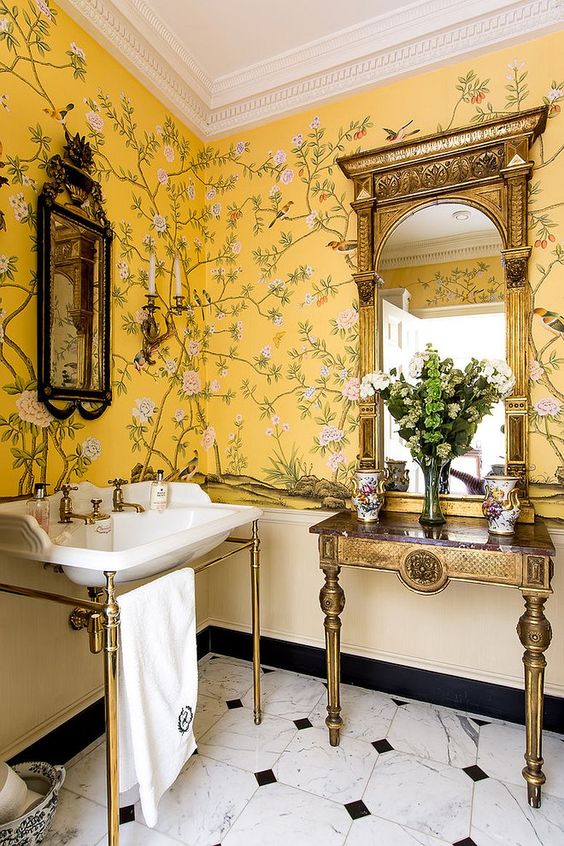 a refined vintage bathroom with beautiful floral wallpaper, a sink on a chic stand, a lovely side table and blooms on it