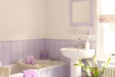 a romantic bathroom with lavender paneling and a mirror, a wooden mat and a vase plus purple towels