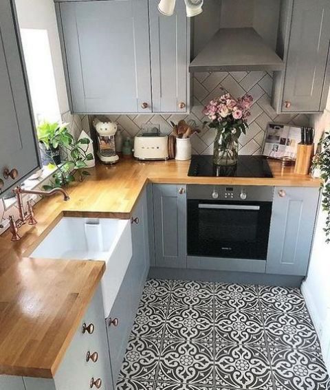 a small farmhouse kitchen done in greys, with a mosaic tile floor, butcherblock countertops and a white tile backsplash done in a chevron pattern