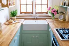 a small pastel farmhouse kitchen with mint cabients, butcherblock countertops, wooden open shelves and a window with wooden framing