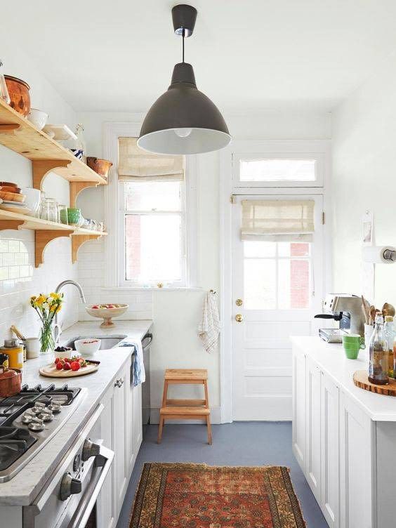 a small rustic kitchen with white cabients, open shelves, a printed rug, a pendant lamp and windows for natural light