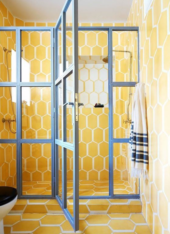 a super bright yellow tile bathroom with a glazed shower door with blue framing for a contrasting look