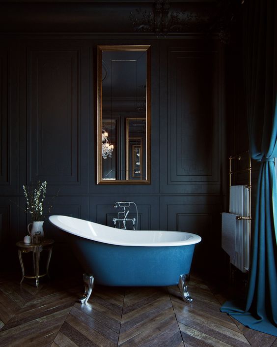 a vintage bathroom with black paneling, a blue clawfoot bathtub, a mirror in a gilded frame, a blue curtain and some brass fixtures