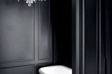 a vintage bathroom with black paneling, a white ceiling, a white bathtub and a crystal chandelier is a chic and lovely space
