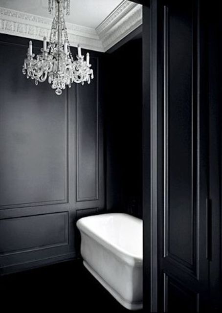 a vintage bathroom with black paneling, a white ceiling, a white bathtub and a crystal chandelier is a chic and lovely space
