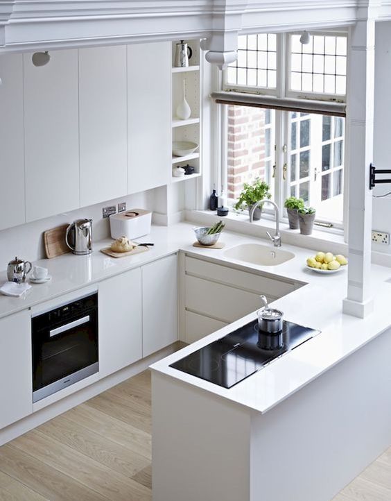 a white minimalist kitchen with sleek cabinets, no handles, a window and simple built-in appliances