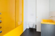 an ultra-minimalist bathroom with a yellow shower space and a vanity with a yellow sink, white walls and a toilet