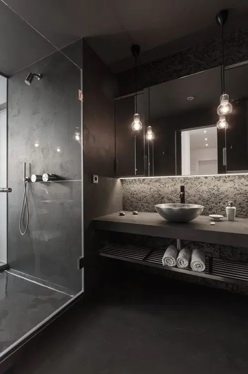 black tiles cover walls all around the bathroom and a stone clad wall adds a textural touch