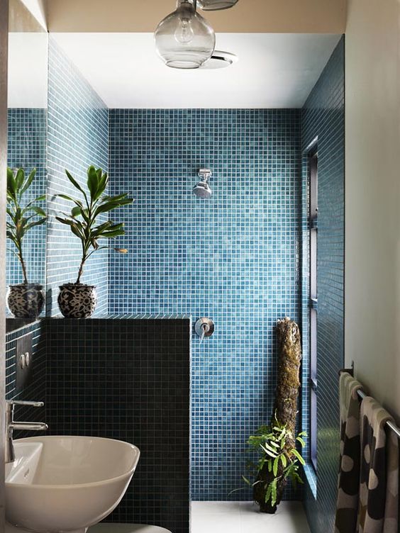 bold blue mosaic tiles in the shower, a half wall, greenery and a vessel sink plus a window for the view