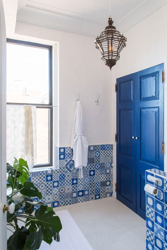 mismatching blue mosaic tiles and a bright blue door with white touches make up a chic and inspiring bathroom