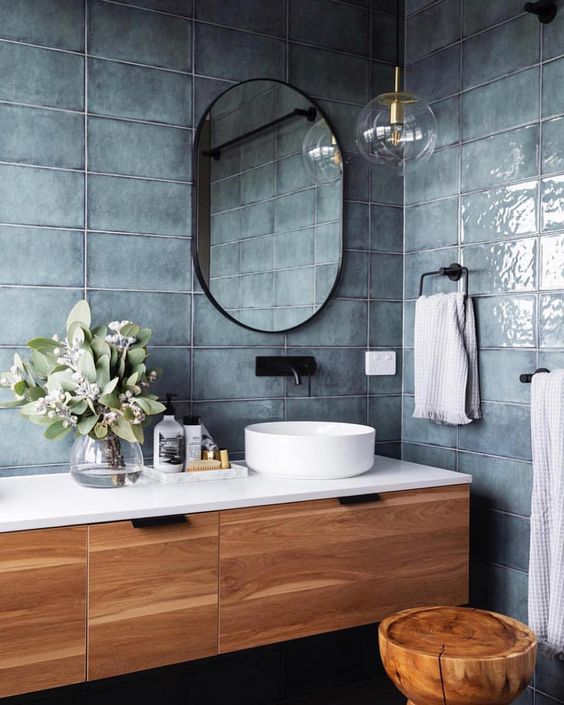slate blue grey tiles, a wooden floating vanity, an oval mirror and a round sink plus a tree stump stool