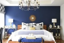 a boho glam bedroom with a navy statement wall and bench, a crystal chandelier, creative nightstands and candles