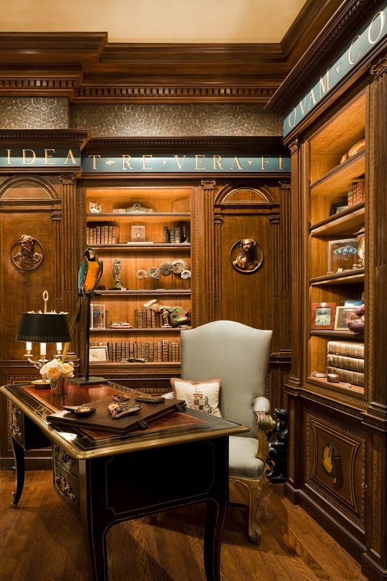 a breathtaking vintage home office with printed wallpaper, stained built-in shelves, a gorgeous dark-stained desk and a grey chair