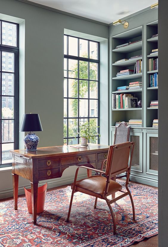 a catchy vintage home office with built-in bookcases, a stained desk and a leather chair, a printed rug and a table lamp