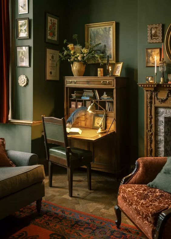 a fab vintage working nook with a stained bureau desk, a table lamp, a green leather chair and some artwork