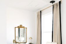 a glam Parisian bedroom in neutrals and black, with a crystal chandelier, a black sideboard, a gold mirror and lamps