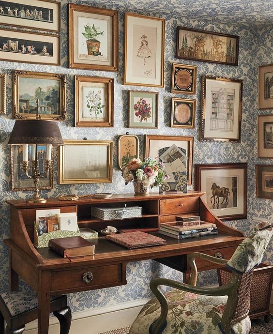 a gorgeous vintage home office with blue floral wallpaper, a fantastic gallery wall and a stained desk plus a floral chair