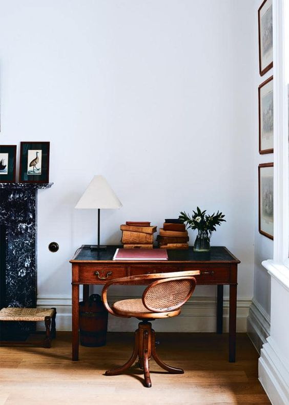 a lovely vintage working nook with a stained desk, a wood and cane chair, a table lamp and stacks of books is a lovely space