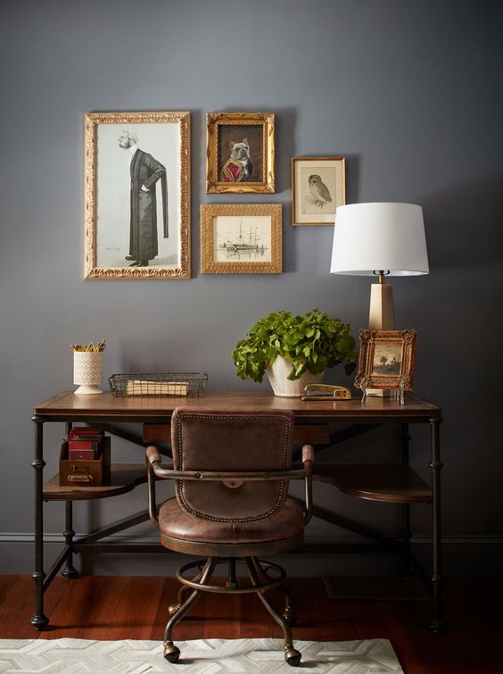 a lovely vintage working space with a chic gallery wall, an industrial desk, a leather chair, a table lamp and potted greenery