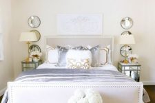 a luxurious glam bedroom in neutrals with a crystal chandelier, mirror nightstands, an upholstered bed, mirrors and a tray