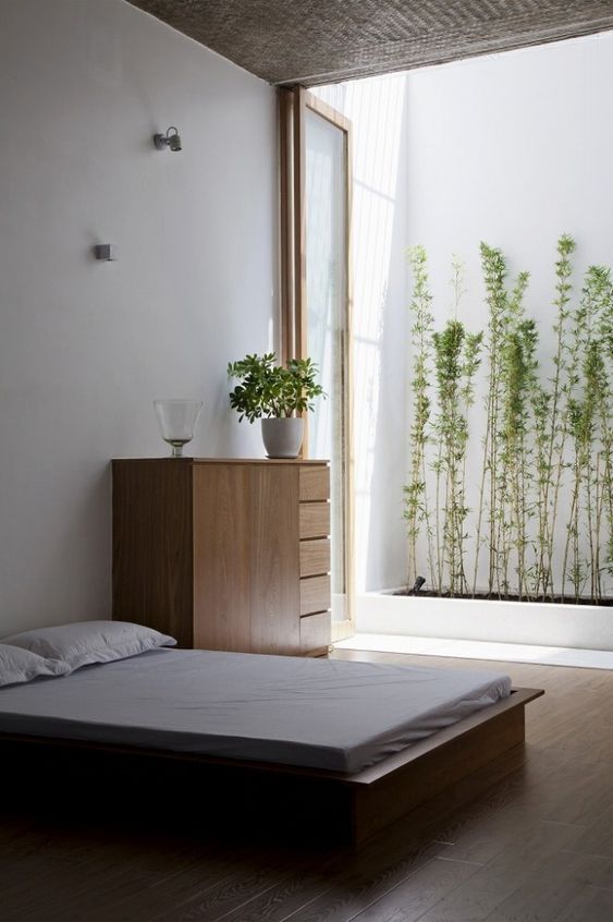 a minimalist zen bedroom with simple wooden furniture, white bedding, some lights connected to a small private garden outdoors