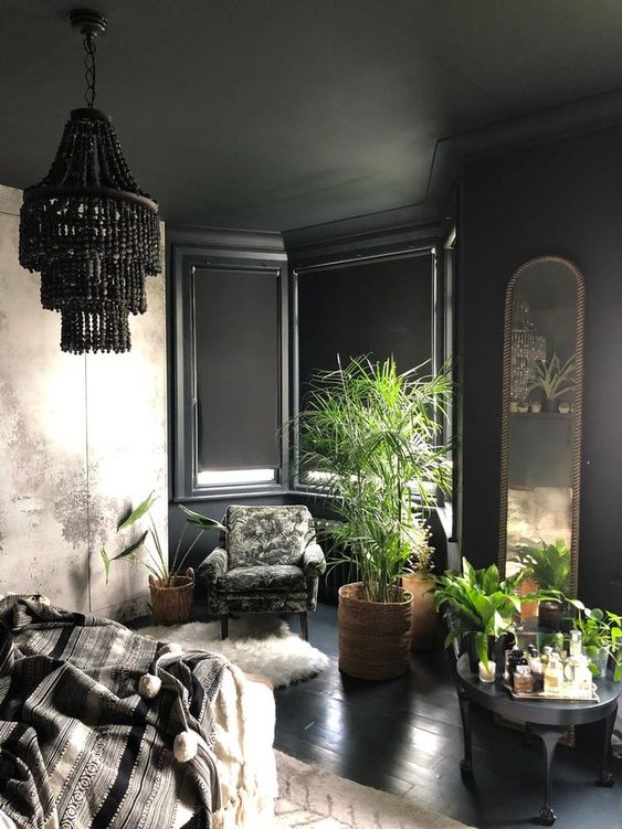 a modern Gothic bedroom with black paneled walls, an abstract print wardrobe, dark furniture, potted plants and a black beaded chandelier