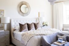 a modern glam bedroom in neutrals, with an upholstered bed, a crystal chandelier, a grey bench, a mirror and rugs