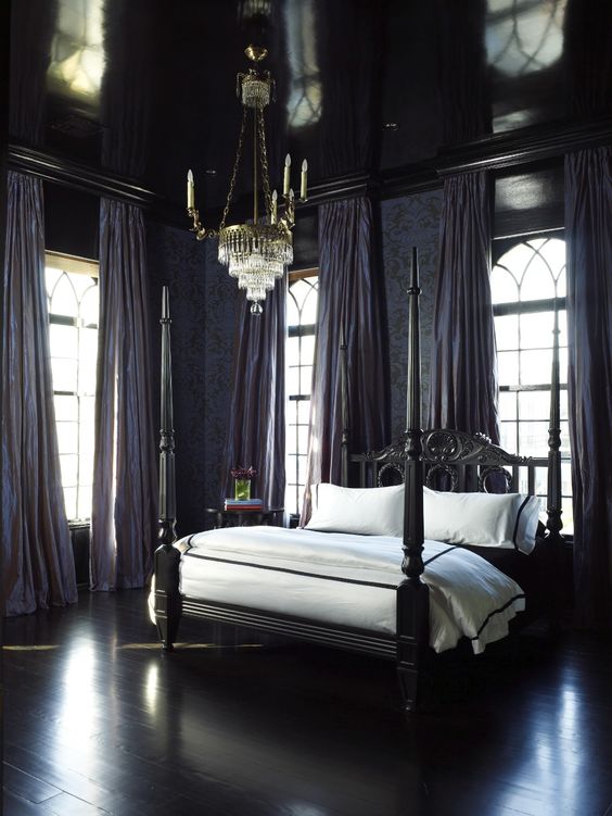 a modern refined Gothic space with grey walls, purple draperies, a carved black bed, a chic crystal chandelier and a glossy ceiling