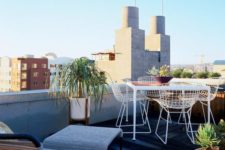 a modern rooftop terrace with a wicker lounger and a footrest, metal furniture, potted plants and a cool view