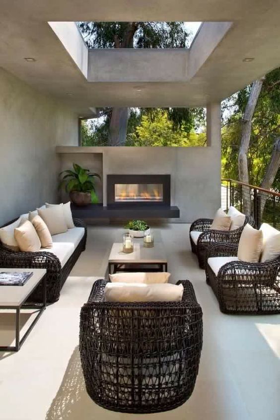 a modern terrace with black wicker furniture, a concrete coffee table, a built-in fireplace and some potted greenery and a skylight