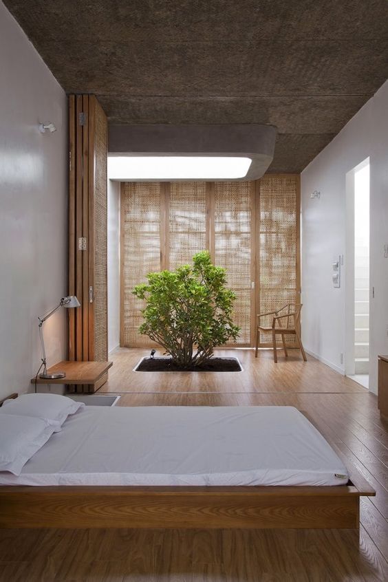 a natural zen bedroom with low wooden furniture, a planted tree, wooden screens and space dividers is a unique space