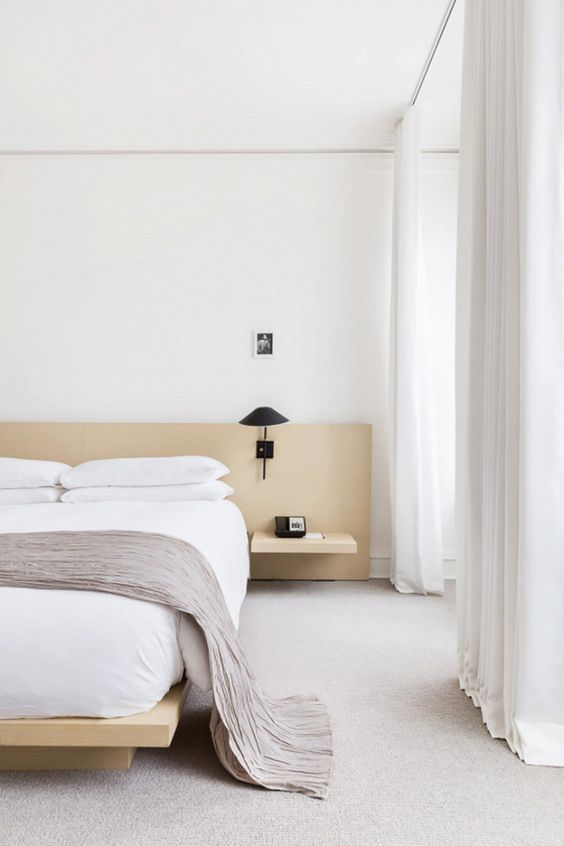 a neutral and welcoming zen bedroom with light-colored wooden bed and nightstands, black sconces and white textiles