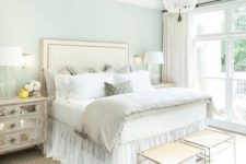 a neutral glam bedroom with an upholstered bed, a crystal chandelier, mirror nightstands and elegant stools