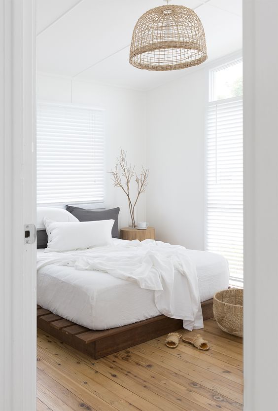 a neutral zen bedroom with a pallet bed, neutral bedding, a woven lamp, a basket and some branches in a vase