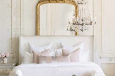 a refined glam bedroom with molding on the walls, a statement mirror, a crystal chandelier and upholstered furniture
