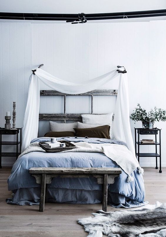 a relaxed zen bedroom with a reclaimed wooden bed, a bench, metal nightstands, blue and grey bedding and a canopy over the bed